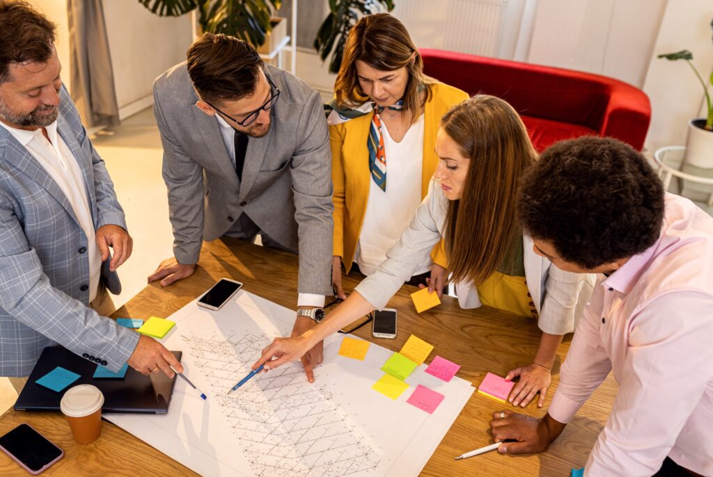 Cinco profesionales de pie alrededor de una mesa analizando un mapa estratégico con post-its de colores en oficina moderna