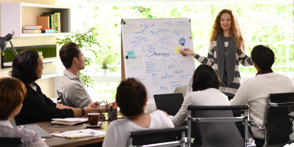 Mujer presentando una estrategia empresarial ante un equipo durante una reunión corporativa en una sala luminosa.