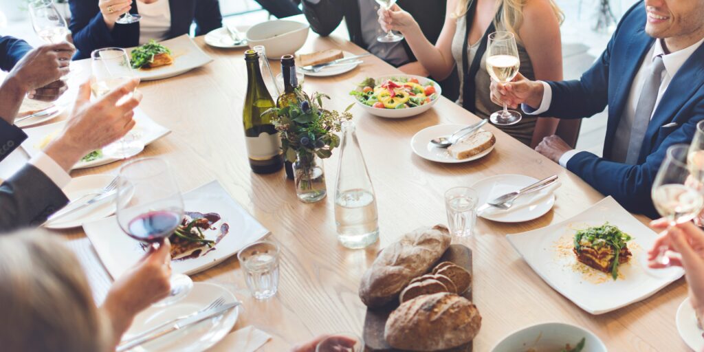 rupo de profesionales compartiendo una comida de networking con vino y platos variados durante un evento corporativo